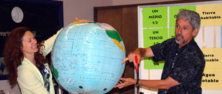 Two adults are holding up a globe and indicating a location